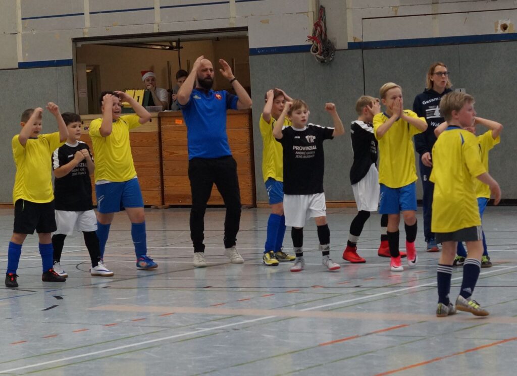 Junge Fußballspieler in gelben und schwarzen Trikots stehen in einer Halle.