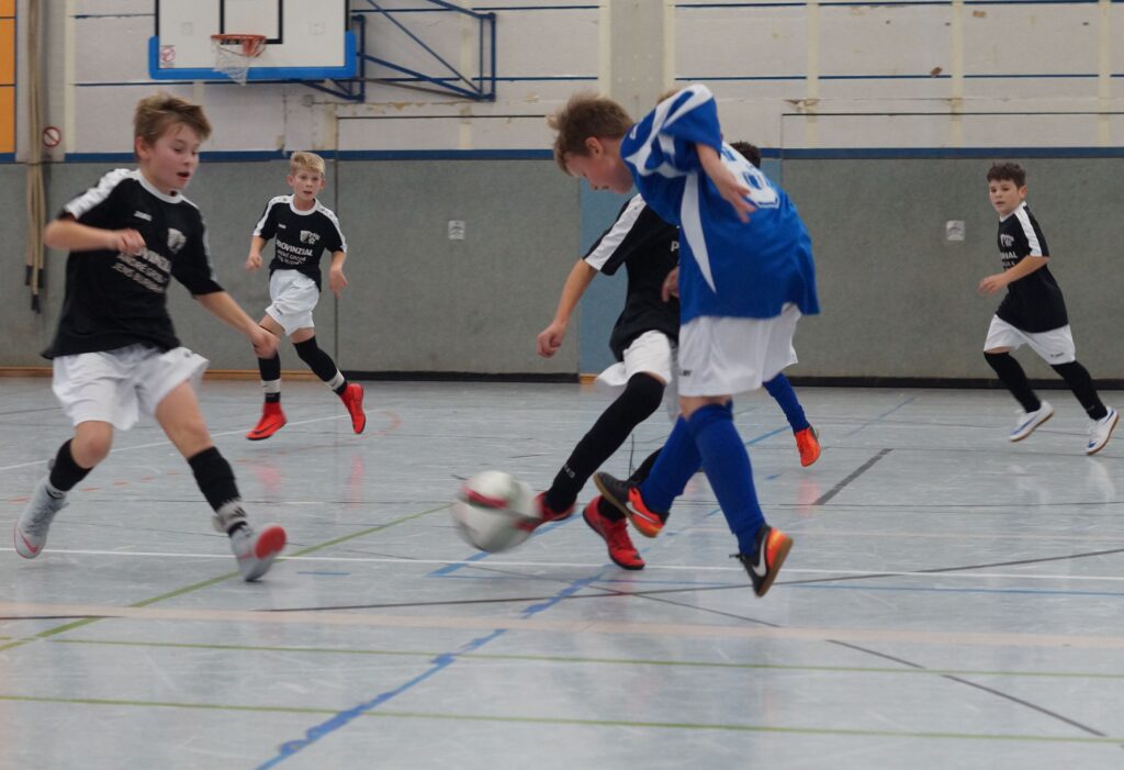 Schnelles Hallenfußballspiel mit Kindern in Sportkleidung.