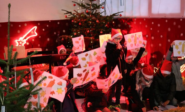 Kinder in Weihnachtsmützen präsentieren Zeichnungen vor einem Weihnachtsbaum.