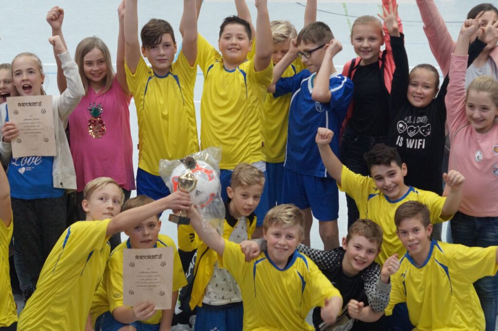 Gruppe von Kindern in Sportkleidung feiert mit Urkunden und einem Fußball.