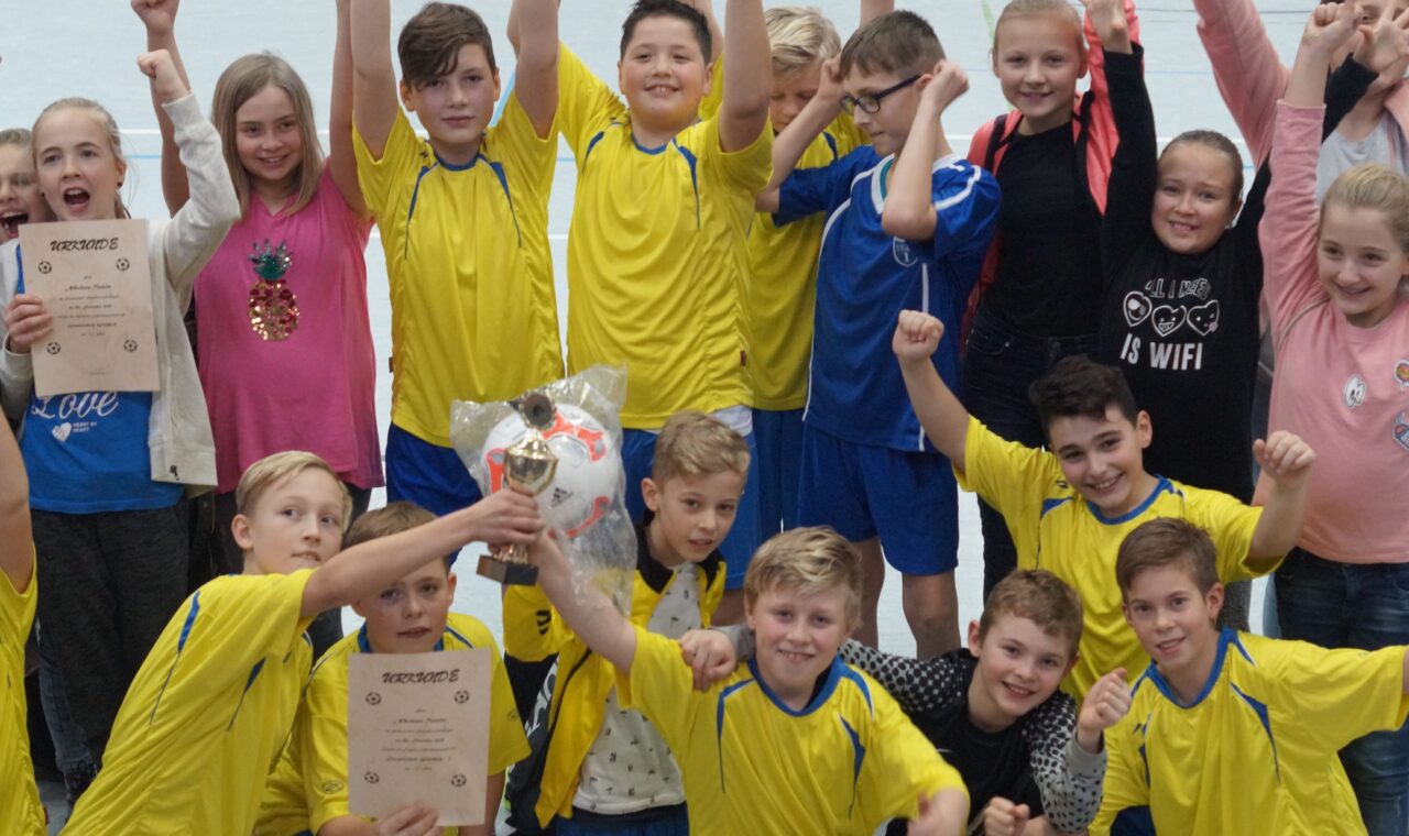Gruppenfoto von Kindern in gelben Trikots, die Pokale und Urkunden feiern.