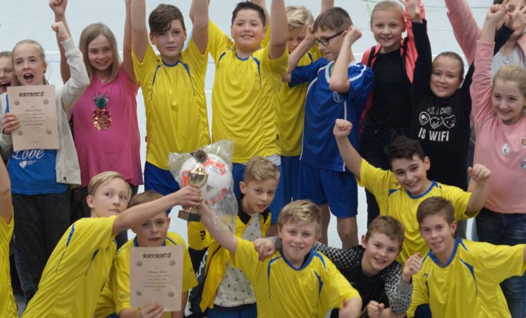 Gruppenfoto von Kindern in gelben Trikots, die Pokale und Urkunden feiern.