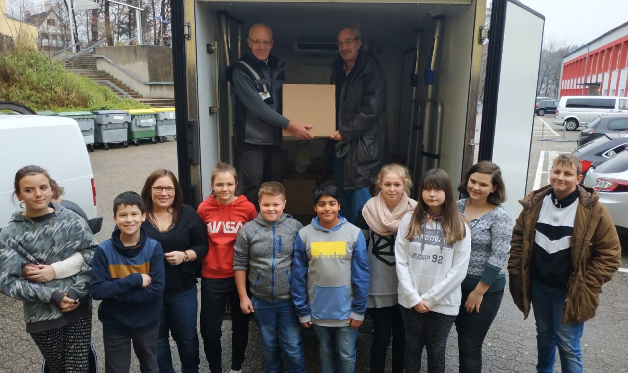 Schülergruppe empfängt eine Box aus einem Lieferwagen.