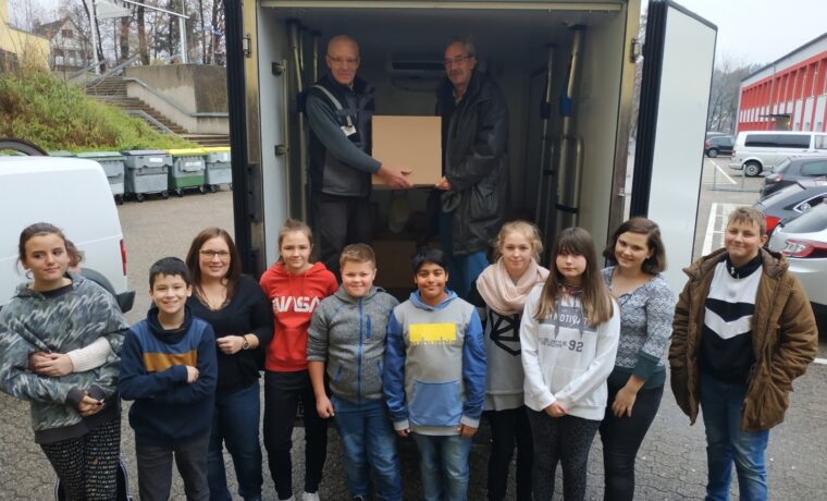 Schülergruppe empfängt eine Box aus einem Lieferwagen.
