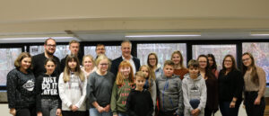 Gruppe von Schülern und Lehrern in einem Klassenraum, lächelnd und stehend.