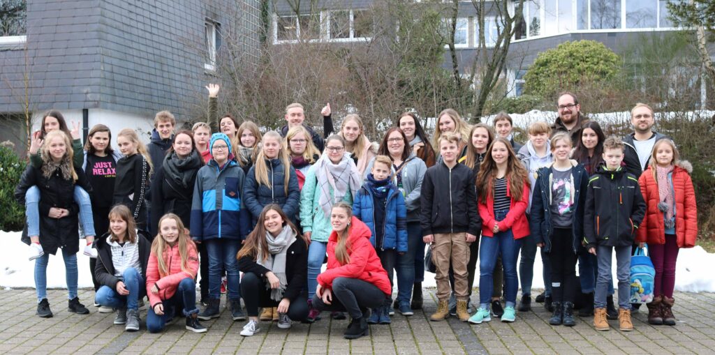 Gruppenfoto von Schülern und Lehrern im Freien, teilweise mit Schnee im Hintergrund.