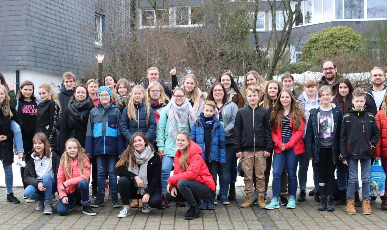 Gruppenfoto von Schülern und Lehrern im Freien, teilweise mit Schnee im Hintergrund.