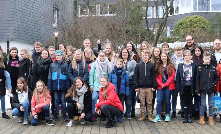 Gruppenfoto von Schülern und Lehrern im Freien, teilweise mit Schnee im Hintergrund.