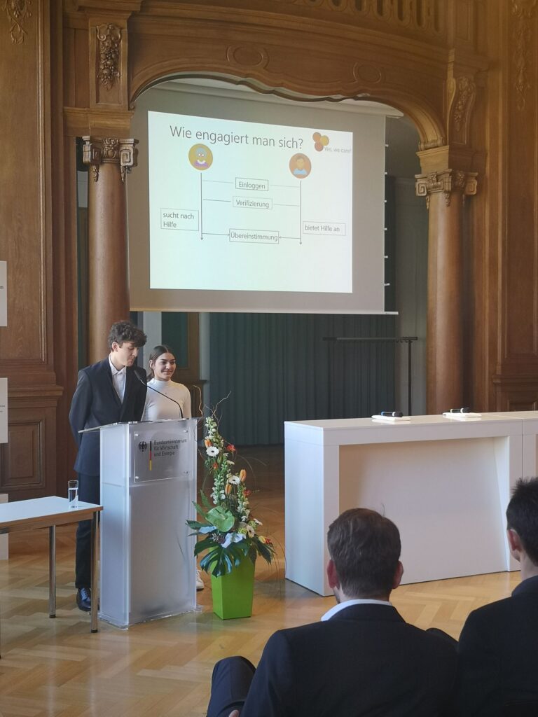 Zwei Personen präsentieren vor einer Präsentationsfolie in einem eleganten Saal.