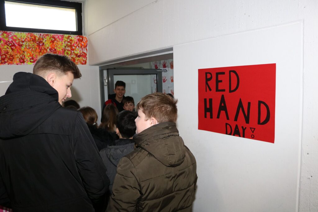 Gruppe von Schülern vor einer Tür mit Plakat "RED HAND DAY".