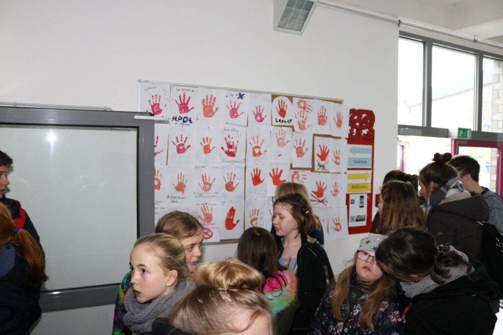 Schüler stehen vor einer Wand mit kreativen Handabdrücken.