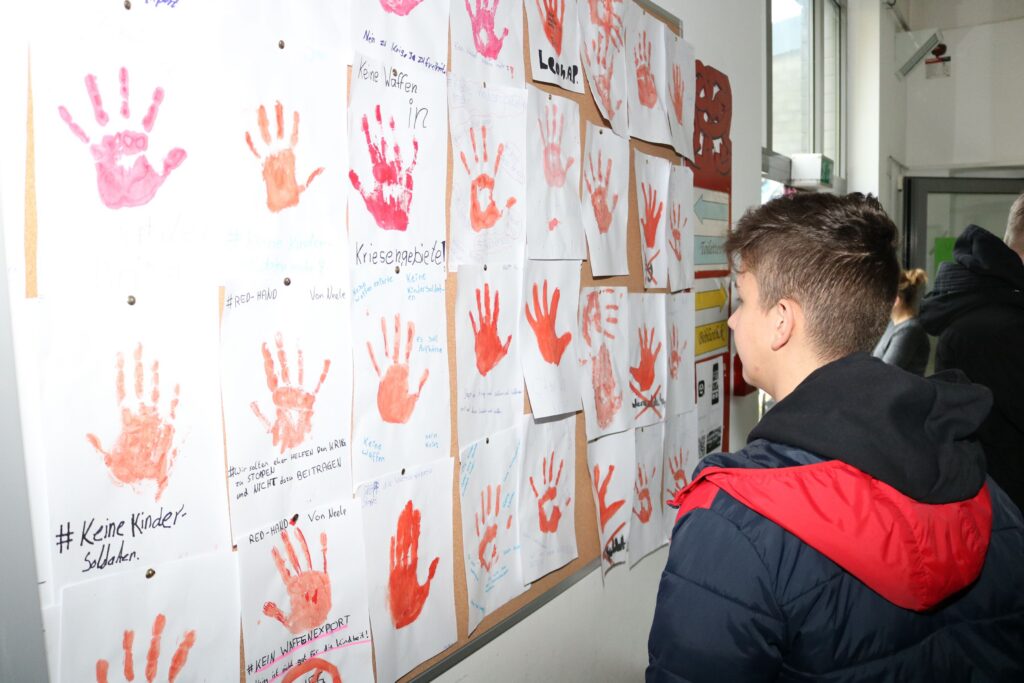 Schüler betrachtet eine Wand mit handabdrückten Kunstwerken.