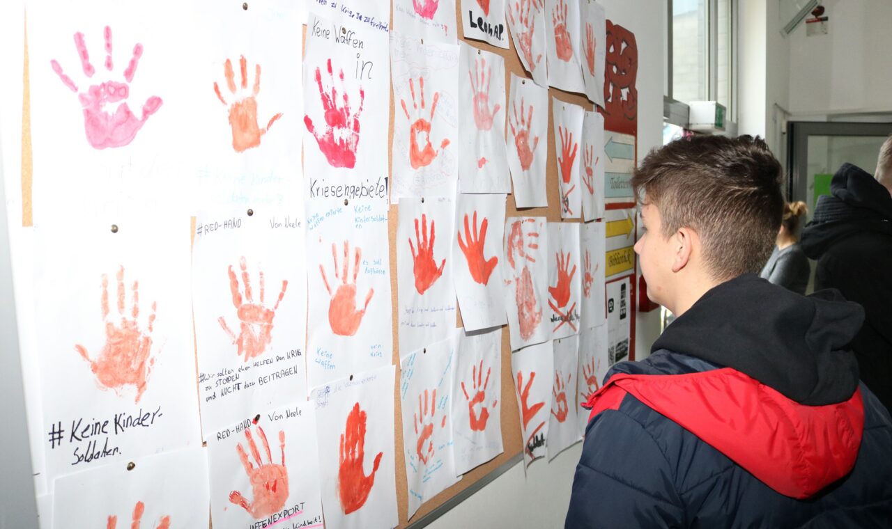 Schüler betrachtet eine Wand mit handabdrückten Kunstwerken.