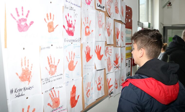 Schüler betrachtet eine Wand mit handabdrückten Kunstwerken.