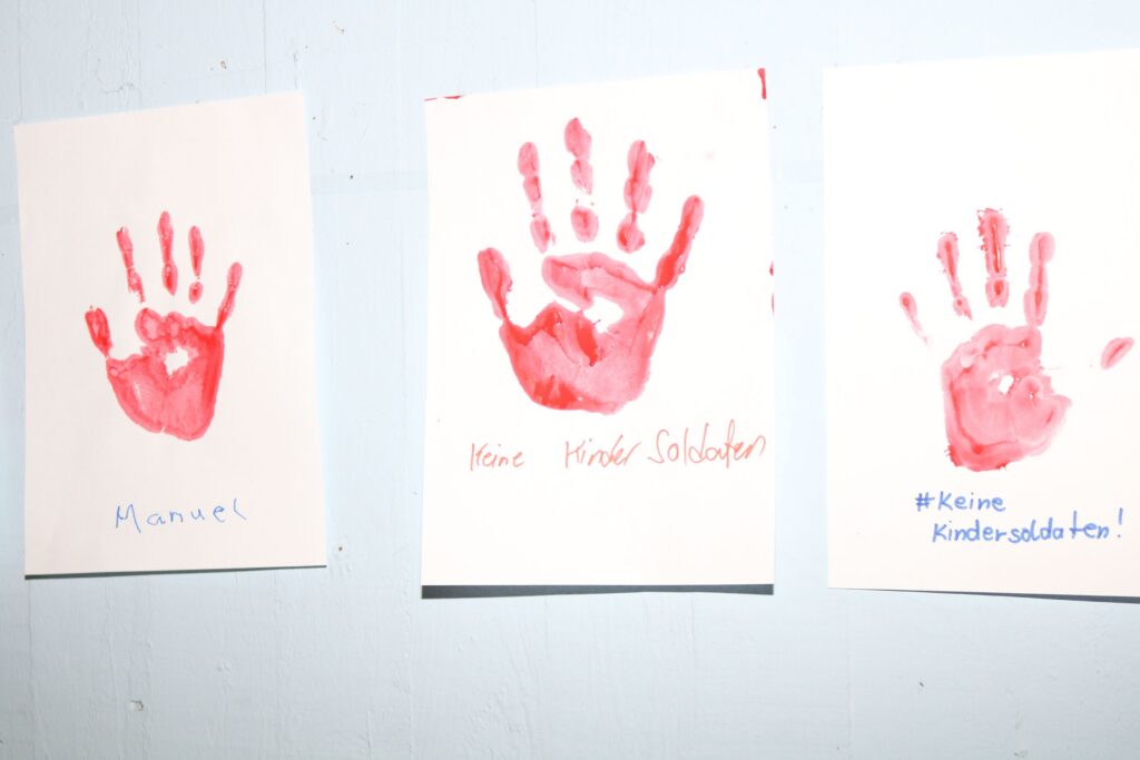 Drei rote Handabdrücke auf Papier mit Beschriftungen.