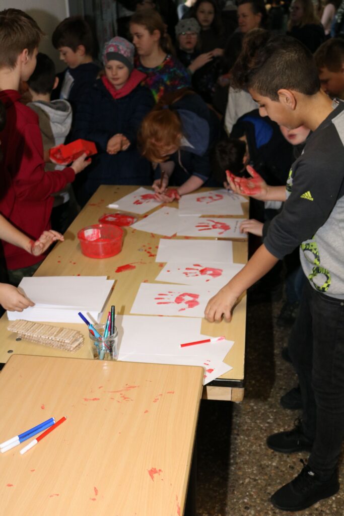 Kinder malen mit roten Farben auf Papier an einem Tisch.