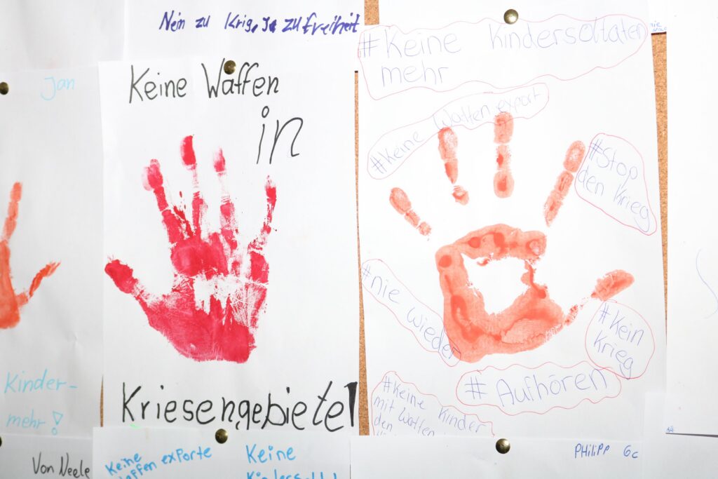 Rote Handabdrücke und Sprüche gegen Waffen auf einem Bulletin Board.