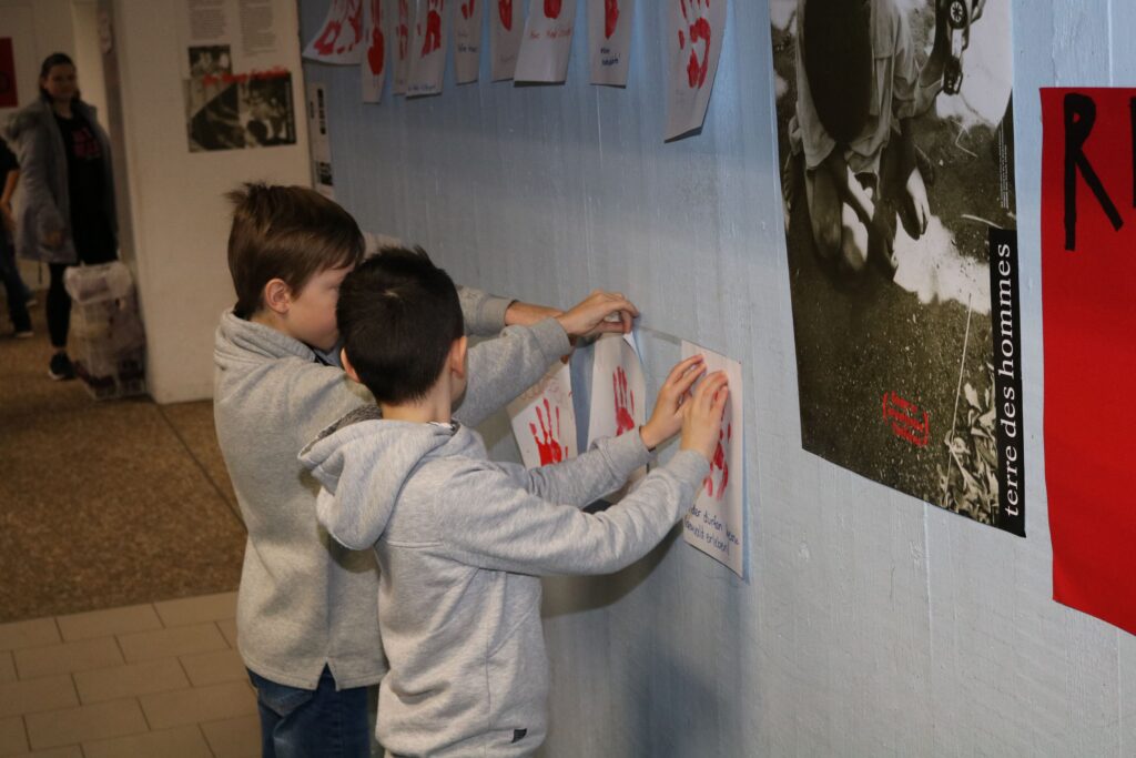 Zwei Jungen kleben Plakate mit roten Handabdrücken an eine Wand.