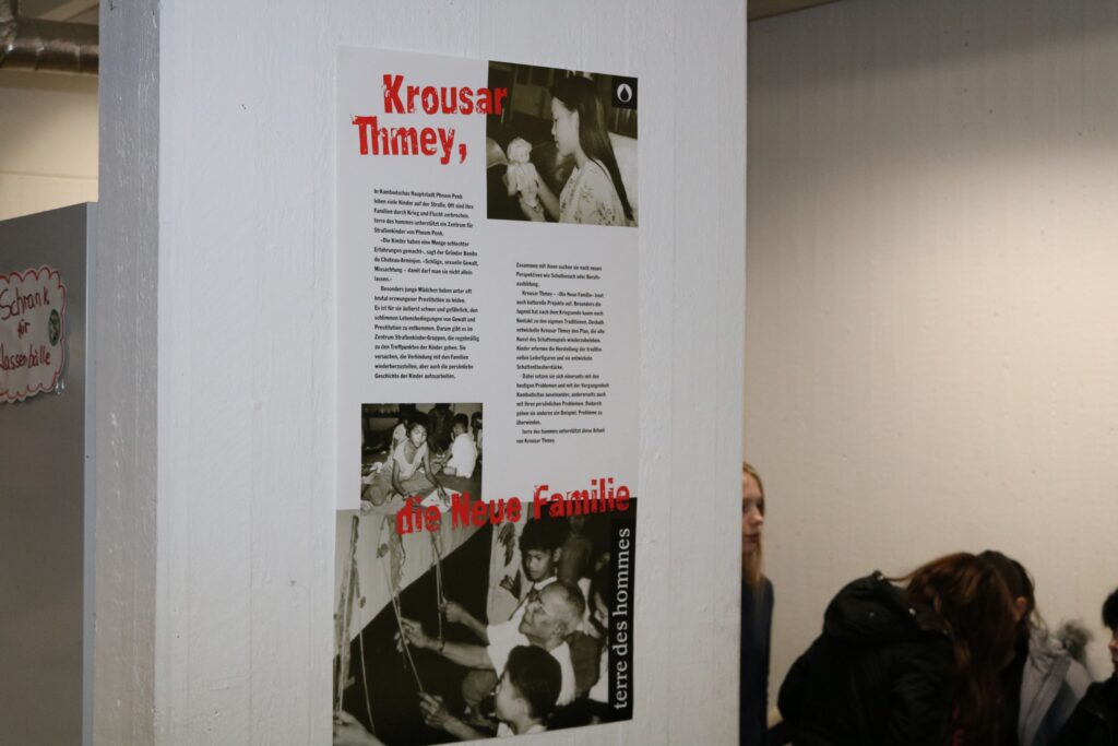 Info-Plakat an einer Wand mit Text und Bildern zur Person Krouser Thiney.