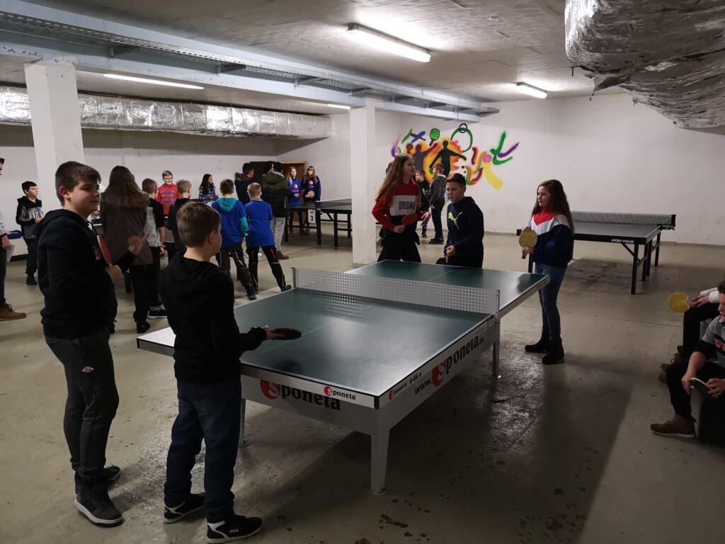 Schüler spielen Tischtennis in einer großen, hellen Sporthalle.