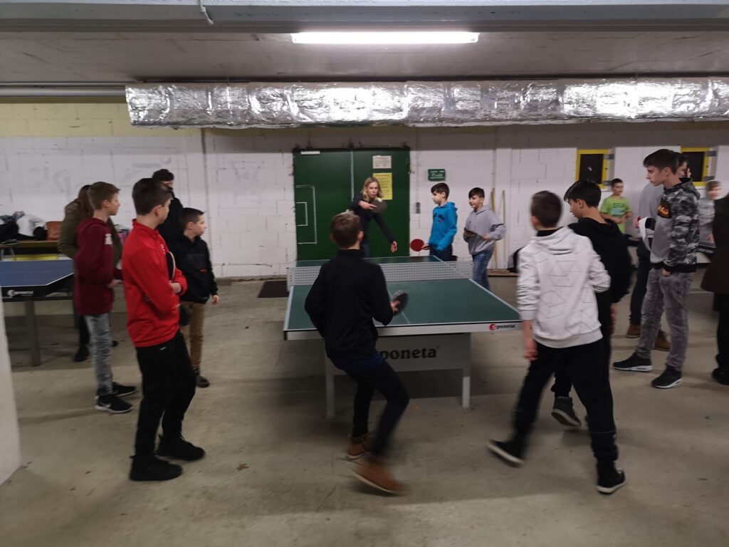 Gruppe von Kindern spielt Tischtennis in einer Sporthalle.
