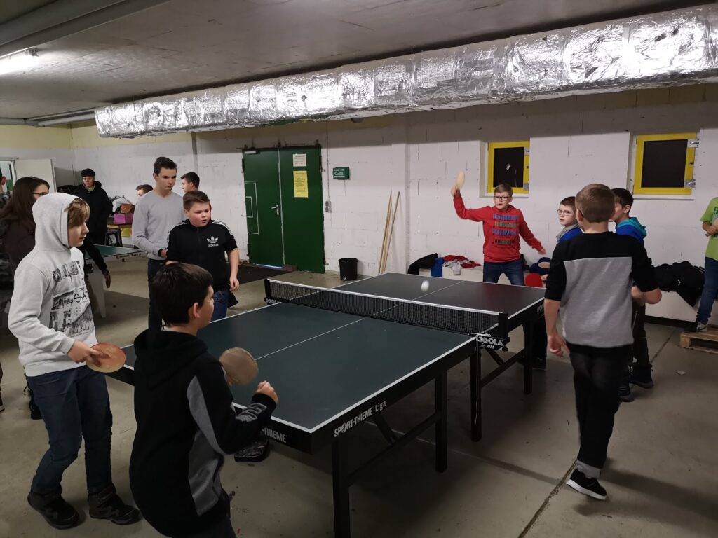 Tischtennisspieler in einer Halle, mehrere Kinder spielen an zwei Tischtennistischen.