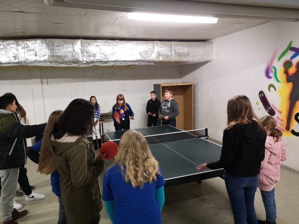 Gruppe von Jugendlichen spielt Tischtennis in einem Raum mit buntem Wandgemälde.