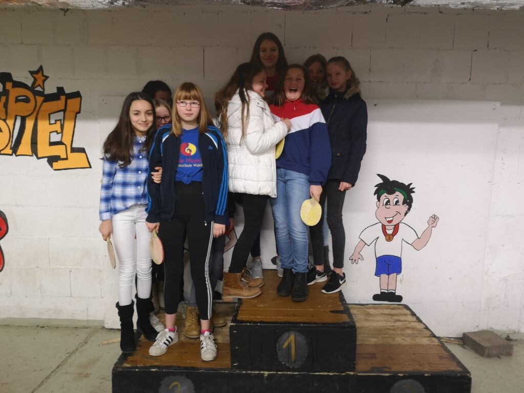 Gruppe von Schülerinnen steht auf dem Siegerpodest vor einer Wand mit Graffiti.