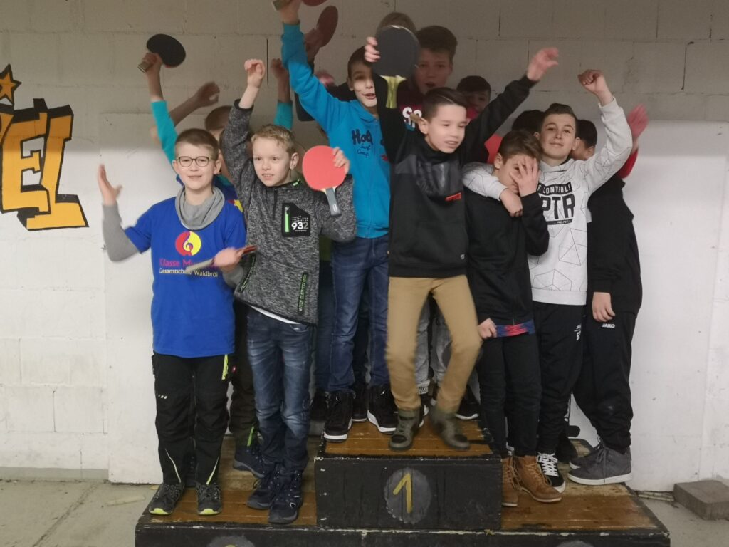 Grupp von Schülern auf einer Siegerehrung, posieren mit Tischtennisplatten.