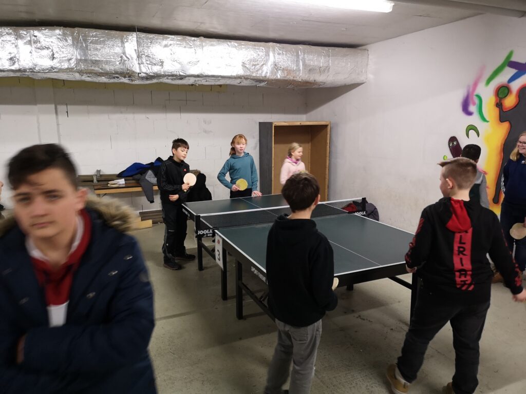 Schüler spielen Tischtennis in einem Raum mit Graffiti an der Wand.