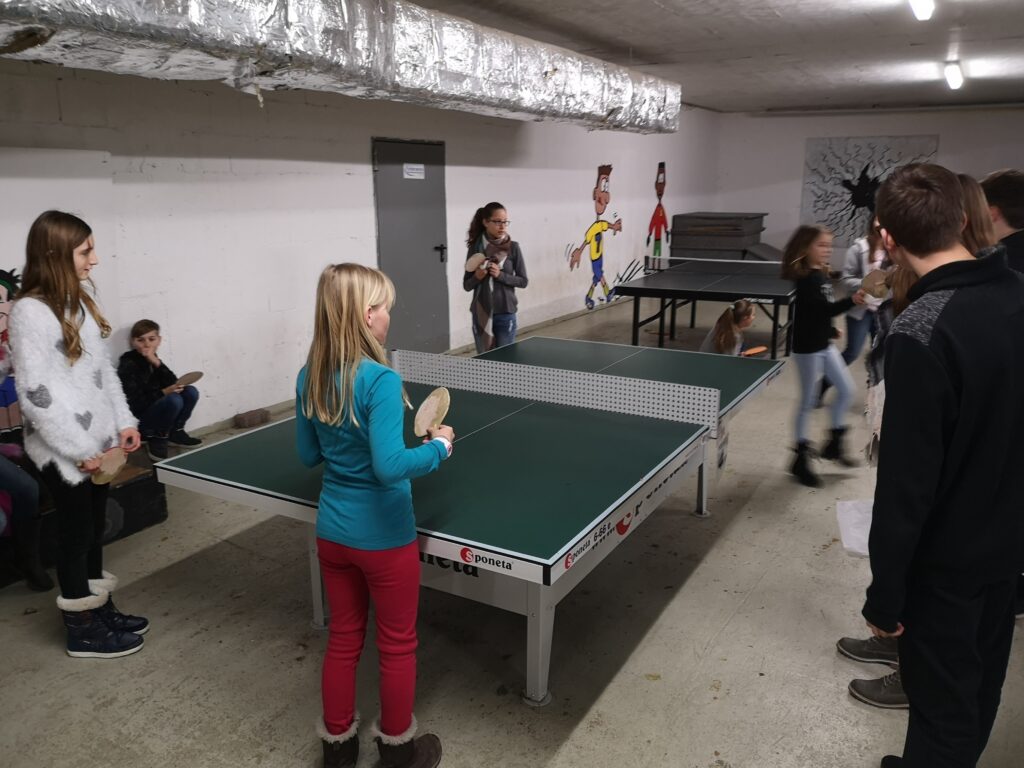 Kinder spielen Tischtennis in einem Kellerraum.