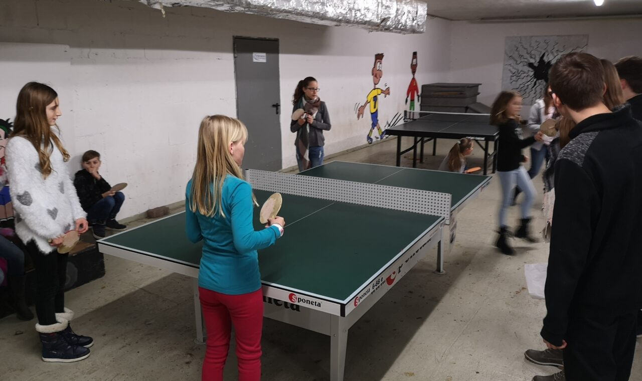 Kinder spielen Tischtennis in einem Kellerraum.