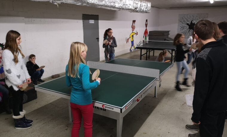Kinder spielen Tischtennis in einem Kellerraum.