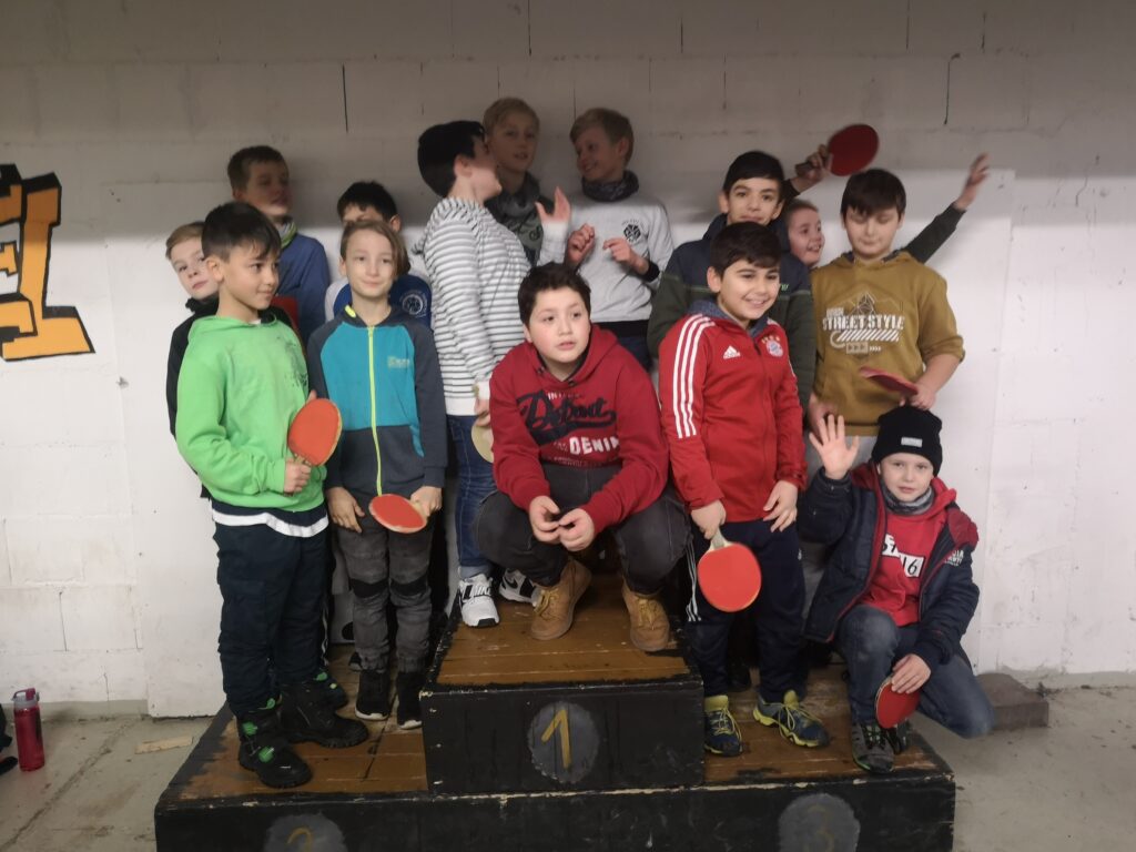 Gruppe von Kindern und Jugendlichen posiert auf einem Treppchen mit Tischtennis-Schlägern.