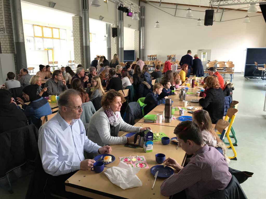 Menschen sitzen an Tischen in einem Raum und essen gemeinsam.