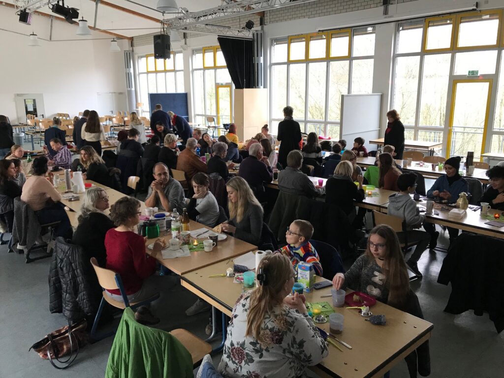 Menschen sitzen an Tischen in einem großen Raum und essen gemeinsam.