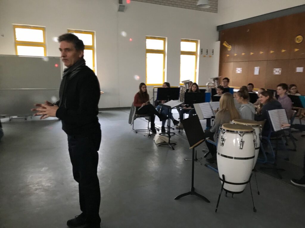 Ein Musiklehrer spricht zu einer Gruppe von Schülern in einem Klassenzimmer.