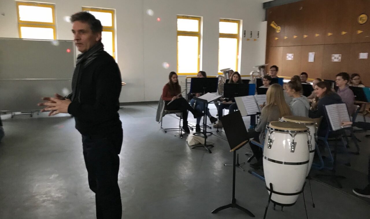 Ein Musiklehrer spricht zu einer Gruppe von Schülern in einem Klassenzimmer.