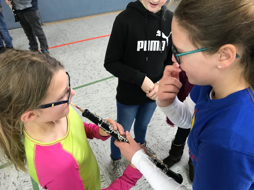 Zwei Mädchen spielen gemeinsam eine Querflöte in der Turnhalle.