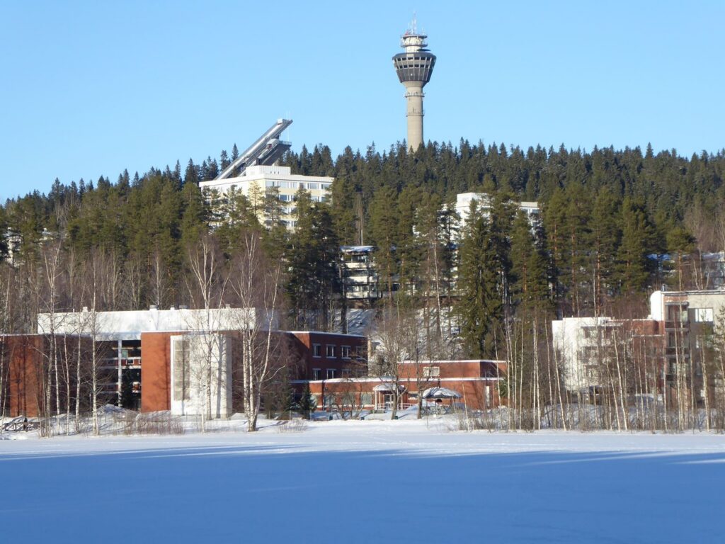 Schneebedeckte Landschaft mit Gebäude und einem Aussichtsturm im Hintergrund.