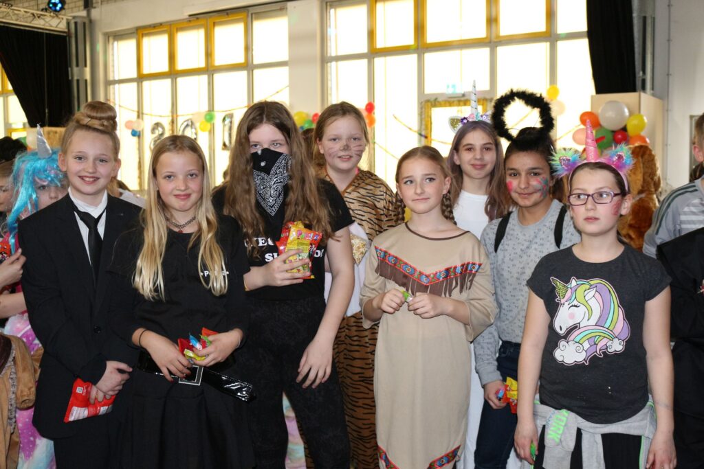 Gruppe von Schülern in Kostümen bei einer Feier in einem Schulraum.