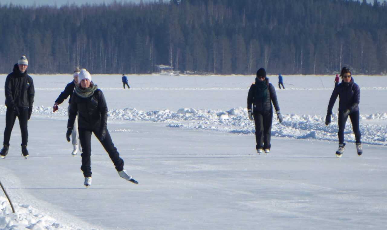Eisläufer auf einem gefrorenen See mit Wald im Hintergrund.