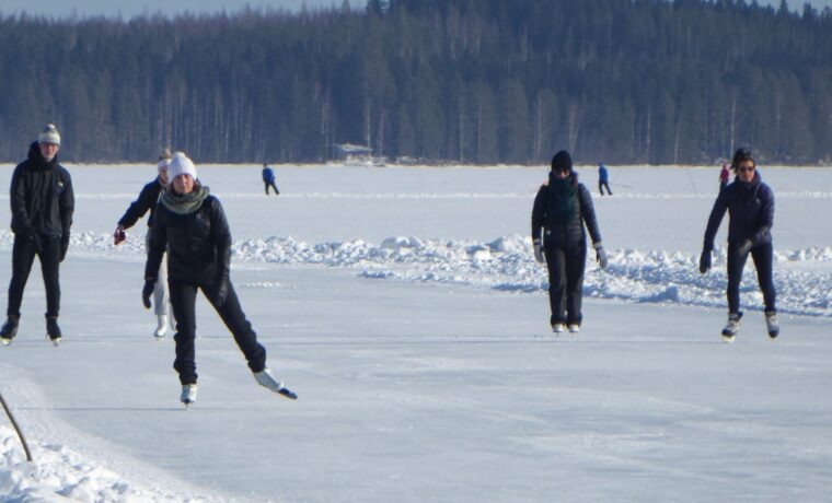 Eisläufer auf einem gefrorenen See mit Wald im Hintergrund.