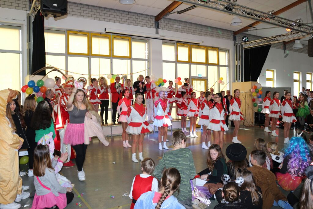 Kinder in Kostümen feiern mit Musik und Dekorationen in einer Halle.
