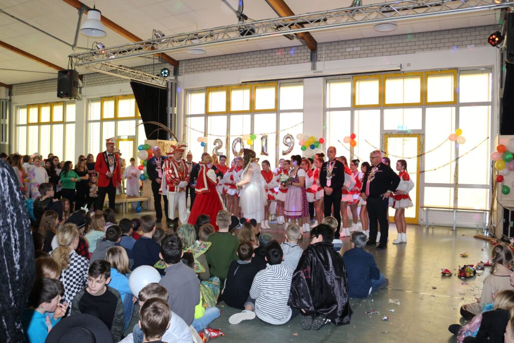 Karnevalsfeier mit verkleideten Personen auf der Bühne und Publikum im Hintergrund.