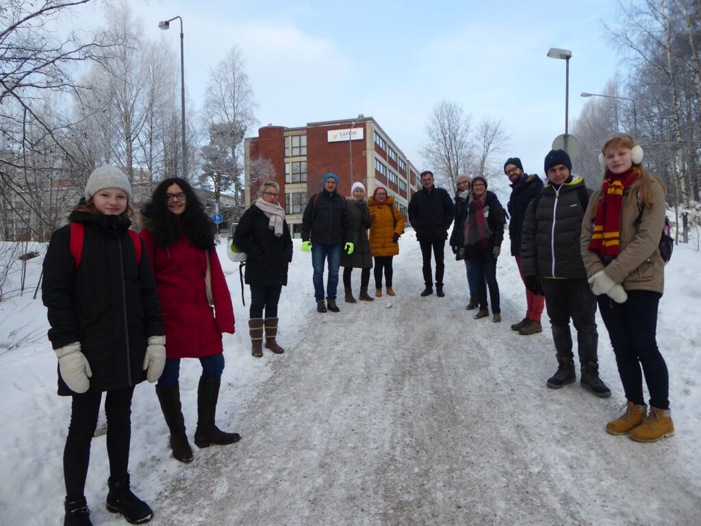 Gruppe von Schülern und Lehrern auf einem schneebedeckten Weg vor einem Schulgebäude.