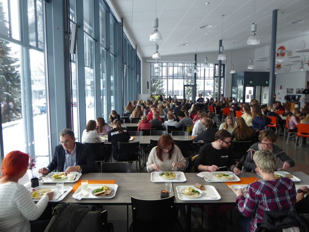Große Mensa mit vielen Menschen, die gemeinsam essen und trinken.