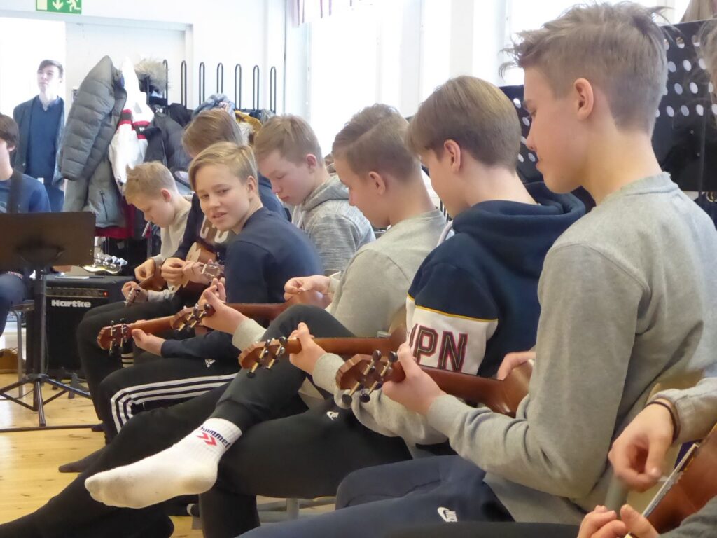 Schüler sitzen in einer Reihe und spielen Ukulele.