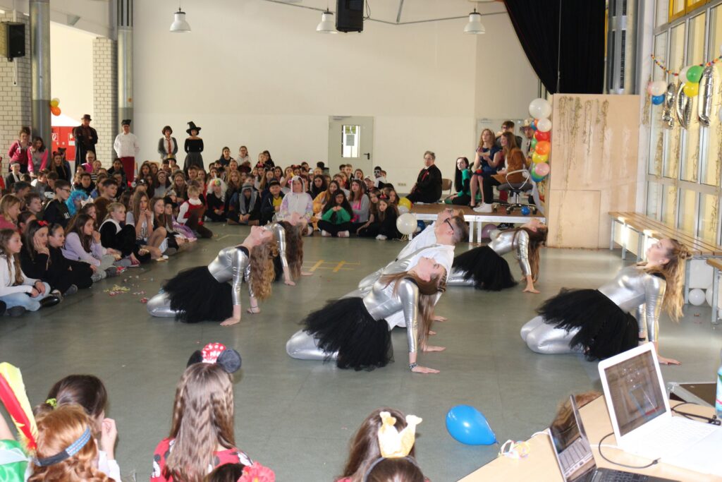 Tanzgruppe in Kostümen führtauffällige Choreografie vor Publikum auf der Schulveranstaltung auf.