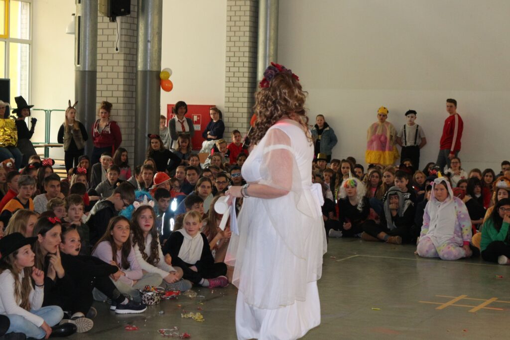 Frau in weißem Kostüm steht auf der Bühne vor einem Publikum.